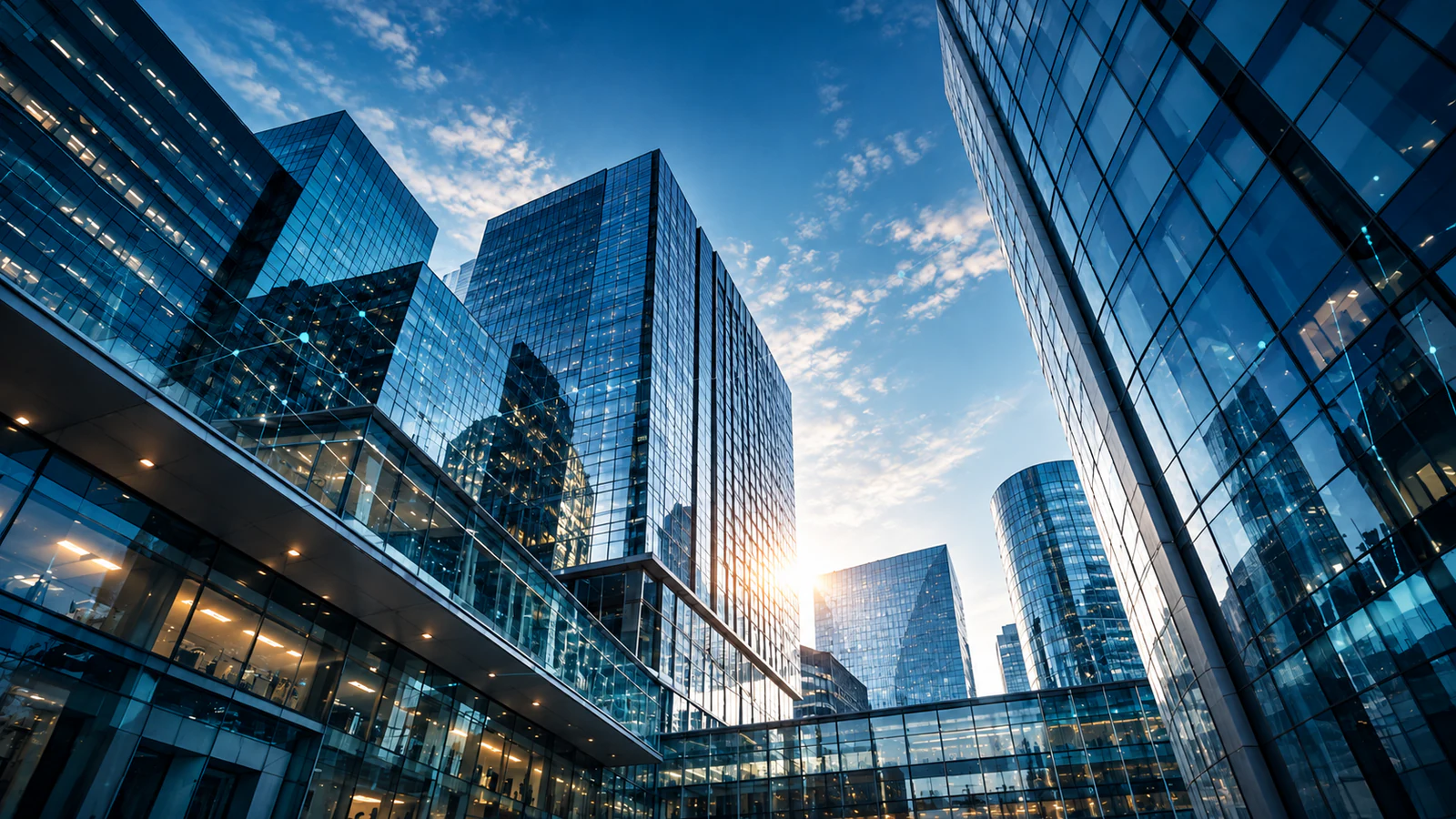 Glass office towers seen from street level, their facades reflecting a bright sky and joined by a glazed bridge.